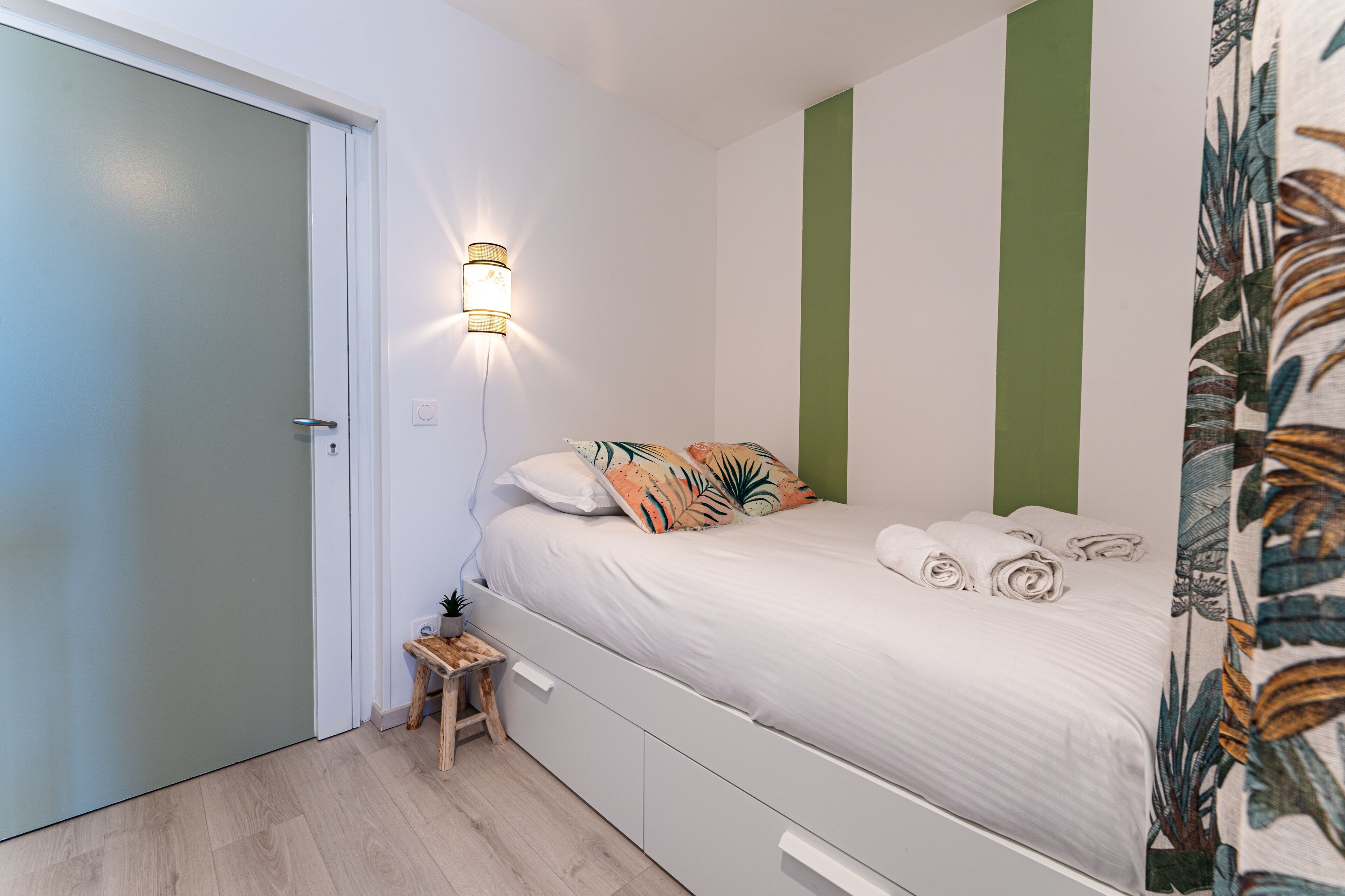 Een slaapkamer met een bed, een nachtkastje, een wandlamp en een groene accentmuur.