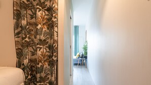 Un couloir étroit, avec un lit sur la gauche et un coin salon comprenant une plante et une petite table, situés au fond.