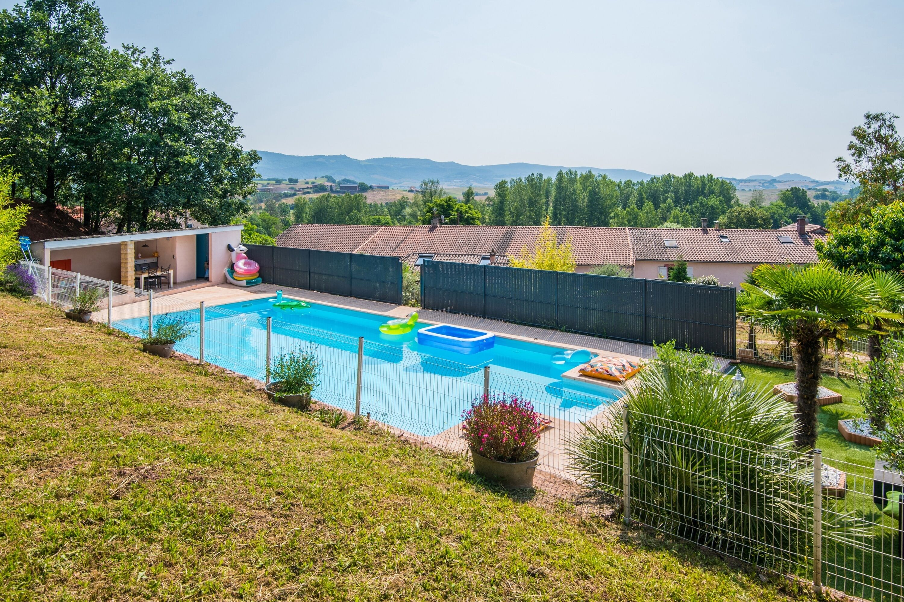 Un patio trasero con piscina, área cercada y vista al campo.