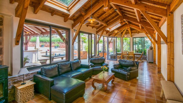 Amplia sala de estar con techo de madera alto, ventanas grandes y una acogedora disposición de asientos.