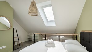 A modern bedroom with a skylight, a bed with white linens, a wooden headboard, and a hanging light fixture. - Le Saint Martin 1 - Bel appartement moderne et confortable (Rennes)