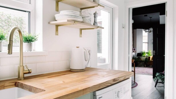 A kitchen with a wooden countertop, a gold faucet, and white cabinets. There are shelves above the counter holding plates and a kettle. - Luxury Designer 4-bed Home in the Heart of Belfast (Belfast)
