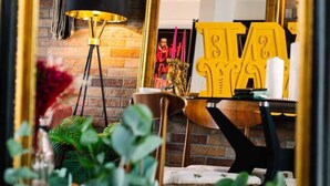 A room with a brick wall, a black floor lamp, a wooden table with yellow letters, and a mirror reflecting the room. - Luxury Designer 4-bed Home in the Heart of Belfast (Belfast)