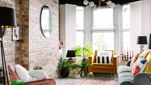 A living room with a brick wall, a round mirror, a yellow armchair, a gray sofa, and a black floor lamp. - Luxury Designer 4-bed Home in the Heart of Belfast (Belfast)