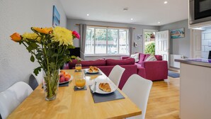 A dining area with a wooden table, chairs, a vase with flowers, plates of food, and a glass of orange juice. - Cornish Holiday - 91 Hengar Manor (St Tudy)
