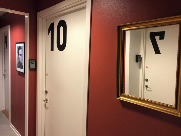 Un pasillo con una puerta marcada con el número 10, un espejo enmarcado y un timbre.