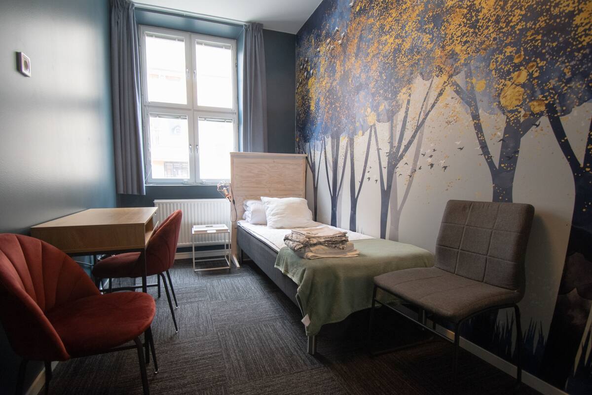 Quarto de hotel com cama, escrivaninha, cadeira e janela.