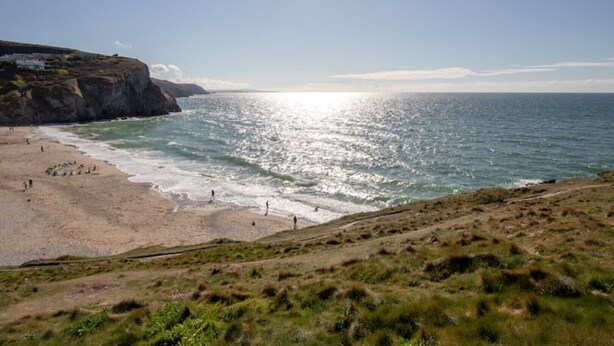 A coastal beach with rocky cliffs, a sandy shore, and a clear sky.
