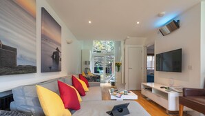 A modern living room with a grey sofa, colorful cushions, a flat-screen TV, and a laptop on a white coffee table.