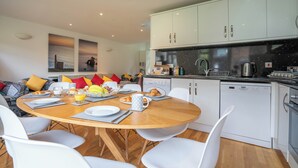A modern kitchen with white cabinets, a black countertop, and a dining area with a wooden table and white chairs.