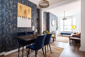 A dining area with a dark wooden table, blue upholstered chairs, and a large painting on the wall. - Luxurious 4-bedroom Home on Trendy Ormeau, Belfast (Belfast)