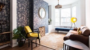 Un salon avec un fauteuil jaune, un canapé marron, un grand miroir et un luminaire suspendu.