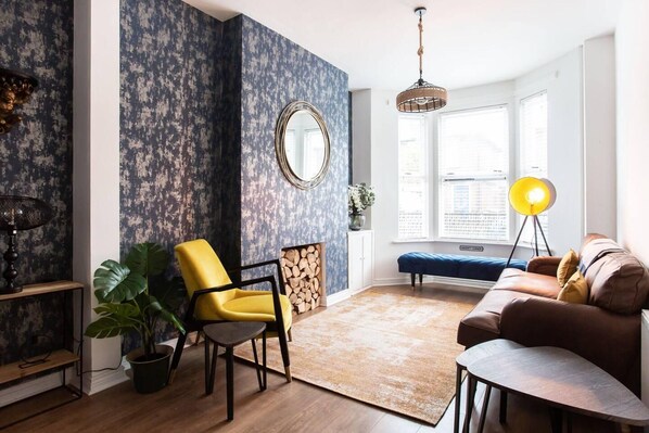A living room with a yellow chair, a brown sofa, a large mirror, and a hanging light fixture. - Luxurious 4-bedroom Home on Trendy Ormeau, Belfast (Belfast)