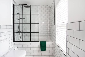 A modern bathroom with white subway tiles, a glass shower enclosure, and a green towel on the floor. - Luxurious 4-bedroom Home on Trendy Ormeau, Belfast (Belfast)