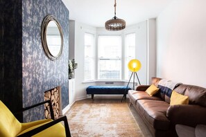 A cozy living room with a brown leather sofa, a yellow chair, a blue accent wall, a large mirror, and a window with a view. - Luxurious 4-bedroom Home on Trendy Ormeau, Belfast (Belfast)