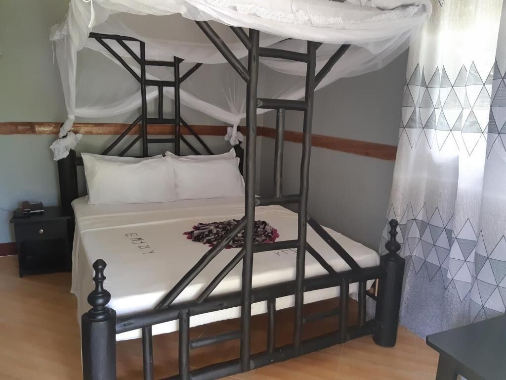 Una cama individual con estructura metálica y dosel, una mesita de noche y una cortina con estampado geométrico.