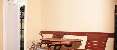 Un comedor con una mesa de madera y dos sillas, una puerta blanca y una estantería con objetos al fondo.