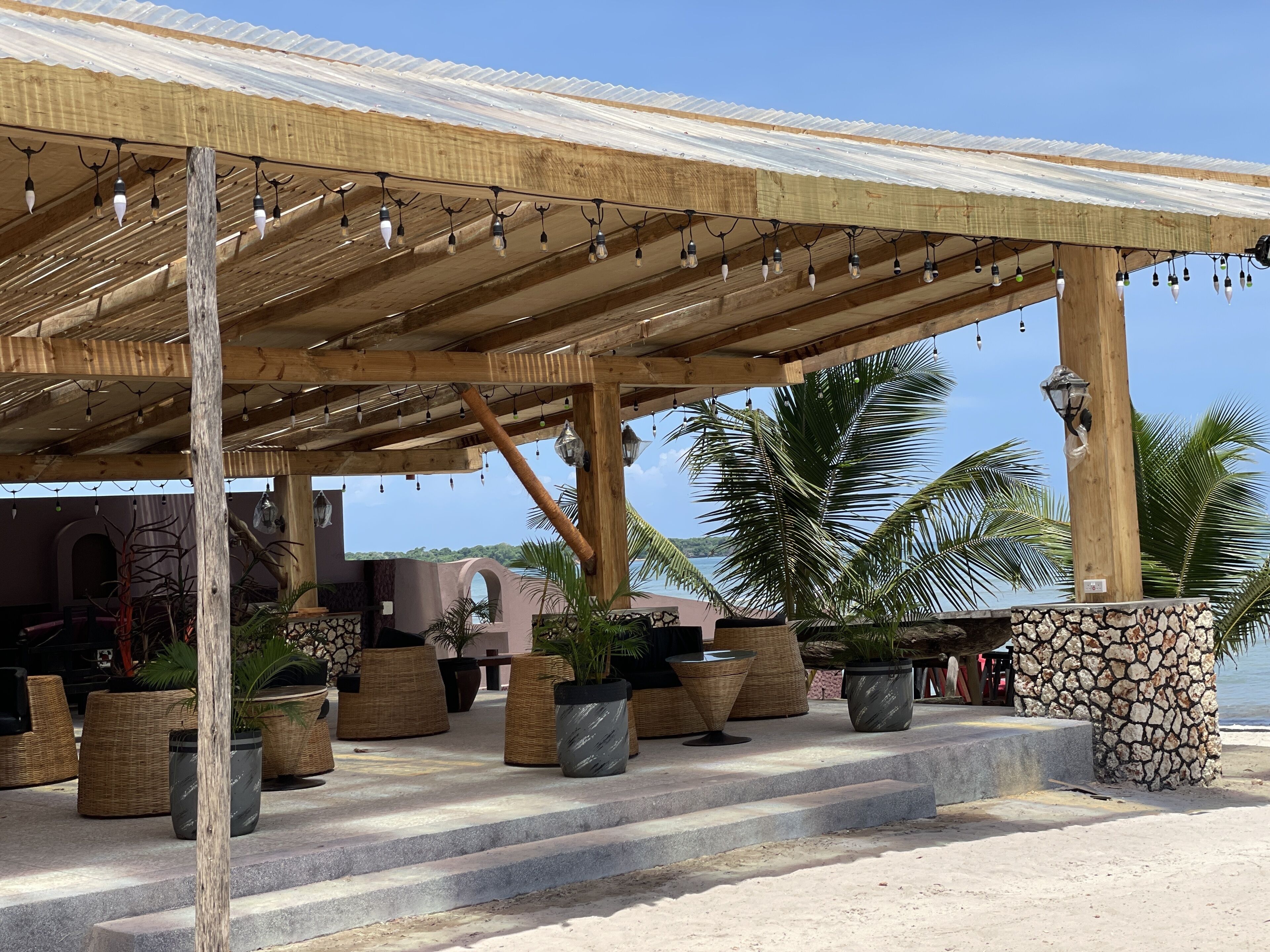 Een overdekt buitengebied met trappen naar een strand, met rieten meubels en potplanten.