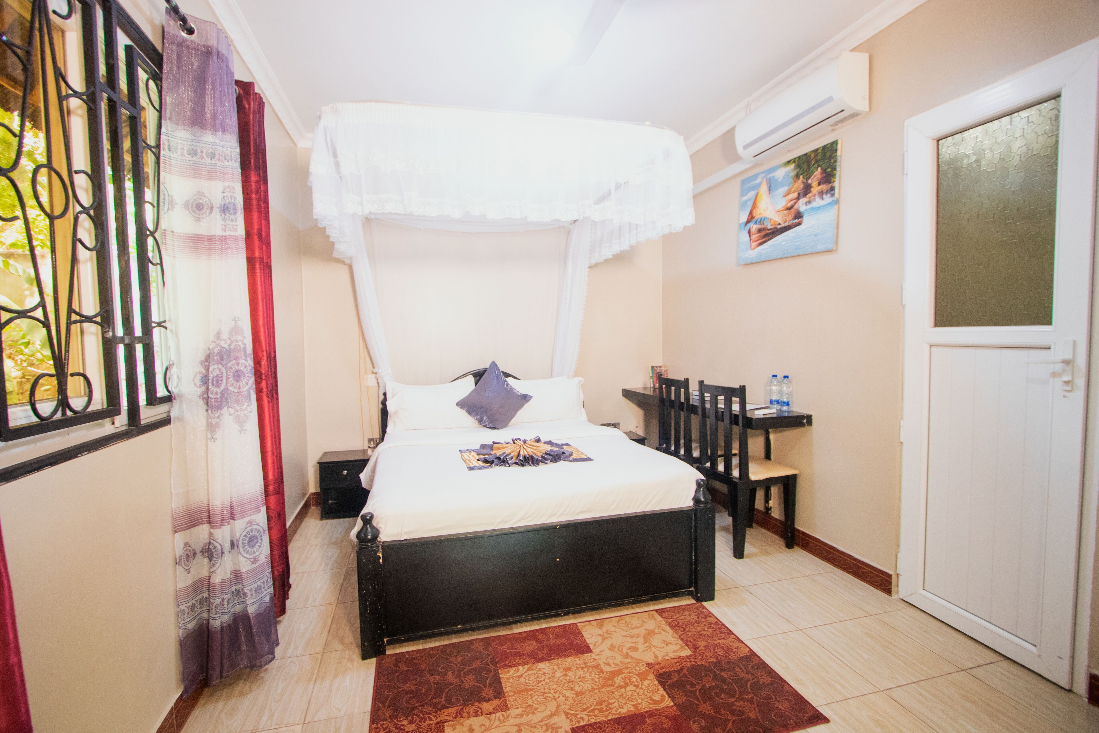 A bedroom with a bed, a chair, a small table, a door, and a window with curtains.