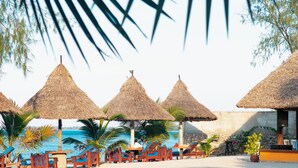 Un complexe hôtelier en bord de mer, doté de parasols à toit de chaume, de chaises longues en bois et offrant une vue sur la mer.