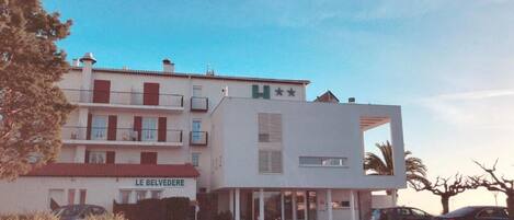 Un hôtel à plusieurs étages, doté d’une façade moderne, de balcons et d’une enseigne indiquant « LE BELVEDERE ».