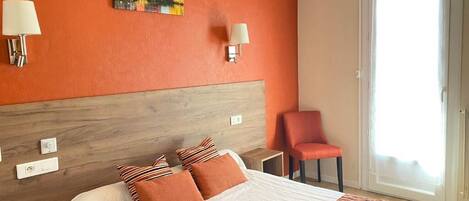 Quarto de hotel com uma cama grande, duas luminárias fixadas na parede, uma cadeira e uma porta de vidro deslizante.