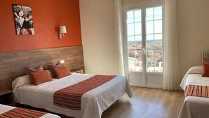Een hotelkamer met twee bedden, een groot raam met uitzicht op de stad, een houten hoofdbord en een wandlamp.