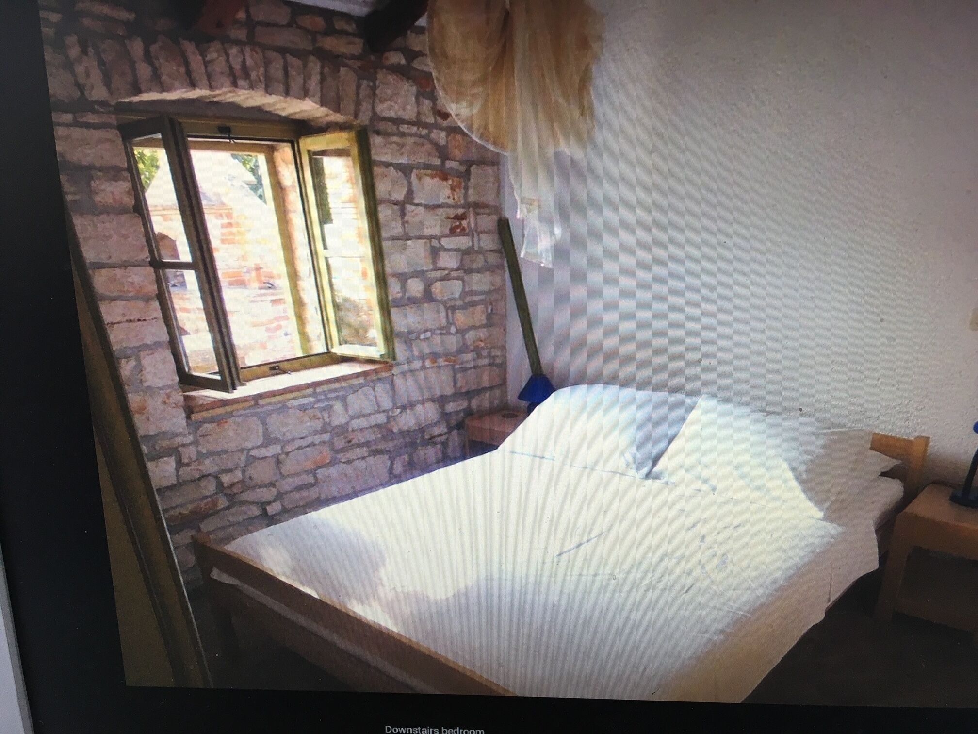 A bedroom with a stone wall, a window, a bed, and a nightstand.