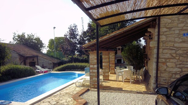 A swimming pool with stone and gravel flooring, a covered patio area with outdoor furniture, and a stone building with a chimney.