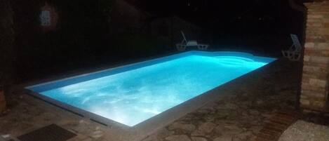 A rectangular swimming pool with a clear blue water surface, surrounded by stone tiles and a brick structure.