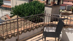 A balcony with a chair, a tiled floor, a metal railing, and a view of the sea and buildings.