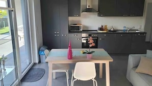 A modern kitchen with dark cabinets, a microwave, oven, and a sink. There is a dining table with two chairs and a potted plant. - Quiet apartment with terrace (Brechen)
