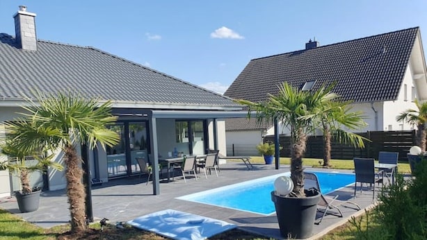 A modern house with a swimming pool, covered patio, and palm trees. - Quiet apartment with terrace (Brechen)