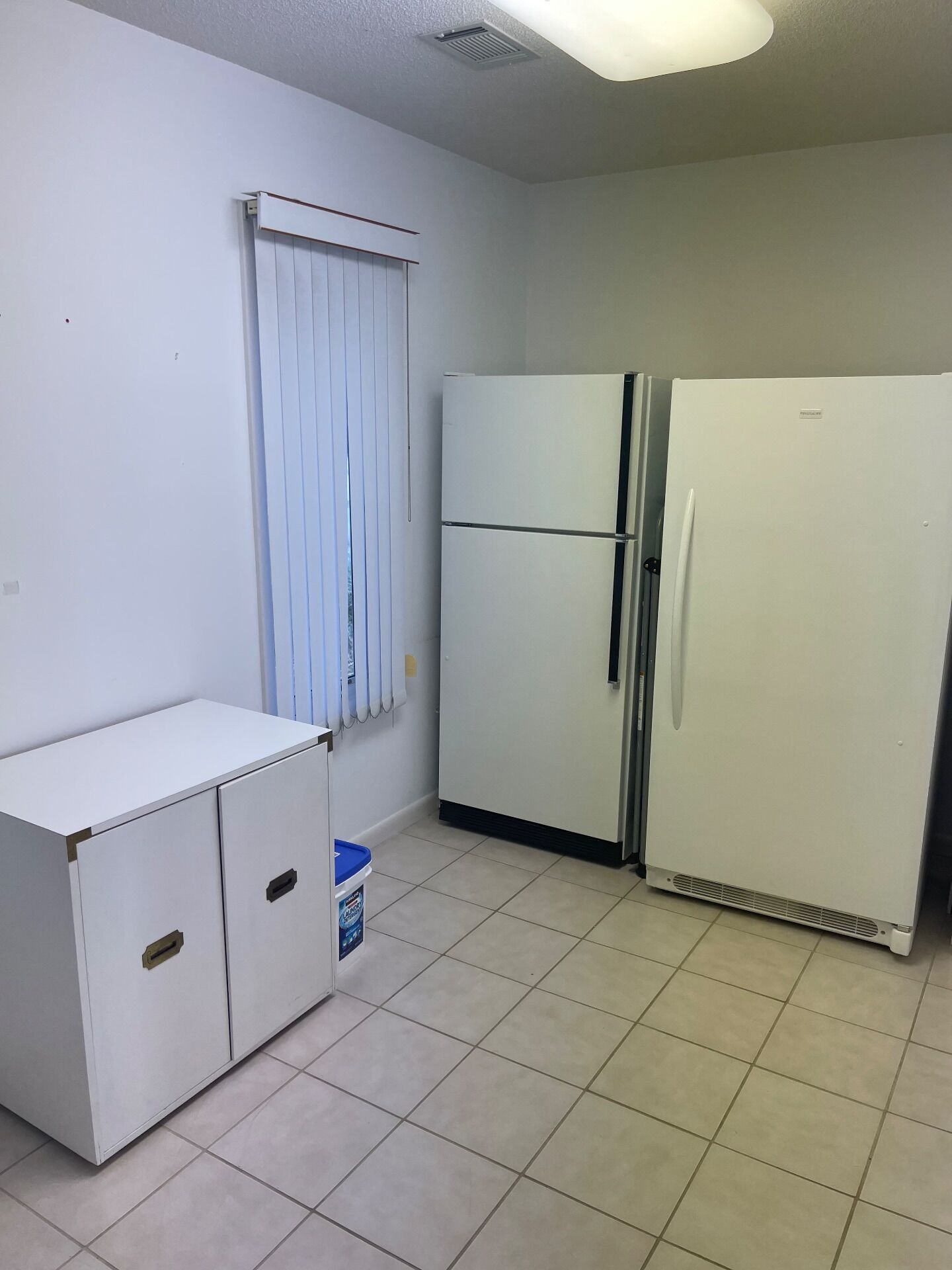 A small kitchen with a white refrigerator, a white cabinet with two drawers, and a blue bucket on the floor.