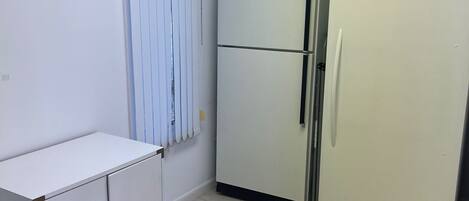 A small kitchen with a white refrigerator, a white cabinet with two drawers, and a blue bucket on the floor.