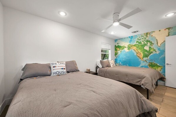 Un dormitorio con dos camas, un ventilador de techo, un mapa mundial en la pared y una almohada con el texto 'THE LAKE HOUSE'.