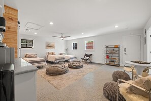 Un dormitorio moderno con dos camas, un ventilador de techo, una pequeña mesa de comedor y una estantería.