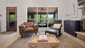 A spacious living room with a large window, leather sofas, a coffee table, and a stone fireplace.