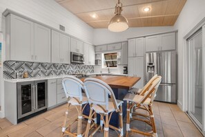 A modern kitchen with white cabinets, a central island with chairs, a microwave, a refrigerator, and a patterned backsplash. - Lakefront Estate: 2 Homes in 1 | Private Dock (Spicewood)