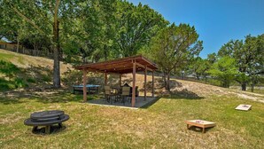 An outdoor pavilion with a table and chairs, surrounded by grass and trees.