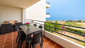 Un balcon avec une table et des chaises, un pot de fleurs et une vue sur la mer et les bâtiments.