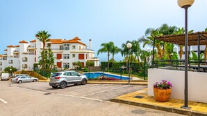 Un parking avec une voiture argentée, une piscine et un bâtiment dont le toit est recouvert de tuiles rouges.
