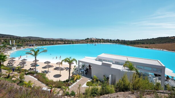 Een resort met een groot zwembad, ligbedden en een wit gebouw met terras.