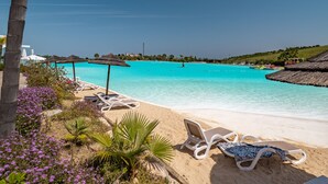 Een strand met helder turquoise water, witte ligbedden en rieten parasols.