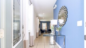 Un pasillo con pared azul, un espejo, una lámpara y un jarrón con flores.