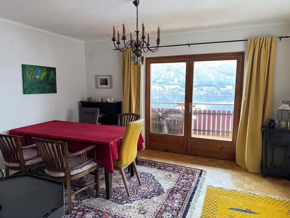 Comedor con una mesa roja, sillas amarillas, un candelabro, vista a un lago a través de una puerta de vidrio y una terraza de madera.