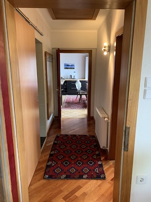 A hallway with a patterned rug, wooden flooring, and a view into a kitchen area with a dining table and chairs.