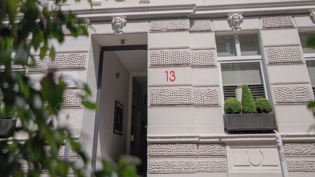 Een wit gebouw met versierde architectonische details, waaronder een balkon met een lamp en een bord met het nummer 13.