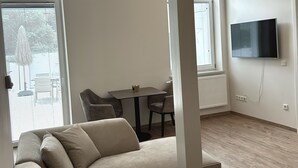 A modern living room with a beige sectional sofa, a dining table with chairs, and a flat-screen TV mounted on the wall. - Pure Highlight Living 9 - Holiday apartment / temporary living (Steinfurt)