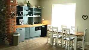 A compact kitchen with a brick column, a wooden dining table with white chairs, and a window providing natural light. - Beautiful 2-bed Apartment Near Waterford City (Waterford)